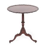 A George III Style Carved Mahogany Tripod Table, the scalloped top above a fluted and carved