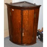 A George III oak bow fronted hanging corner cupboard