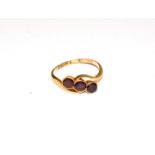 A garnet three stone twist ring, round cut garnets in yellow millegrain settings, on a twist