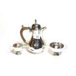 A George V silver hot water jug and associated cream jug and sugar bowl, the hot water jug by