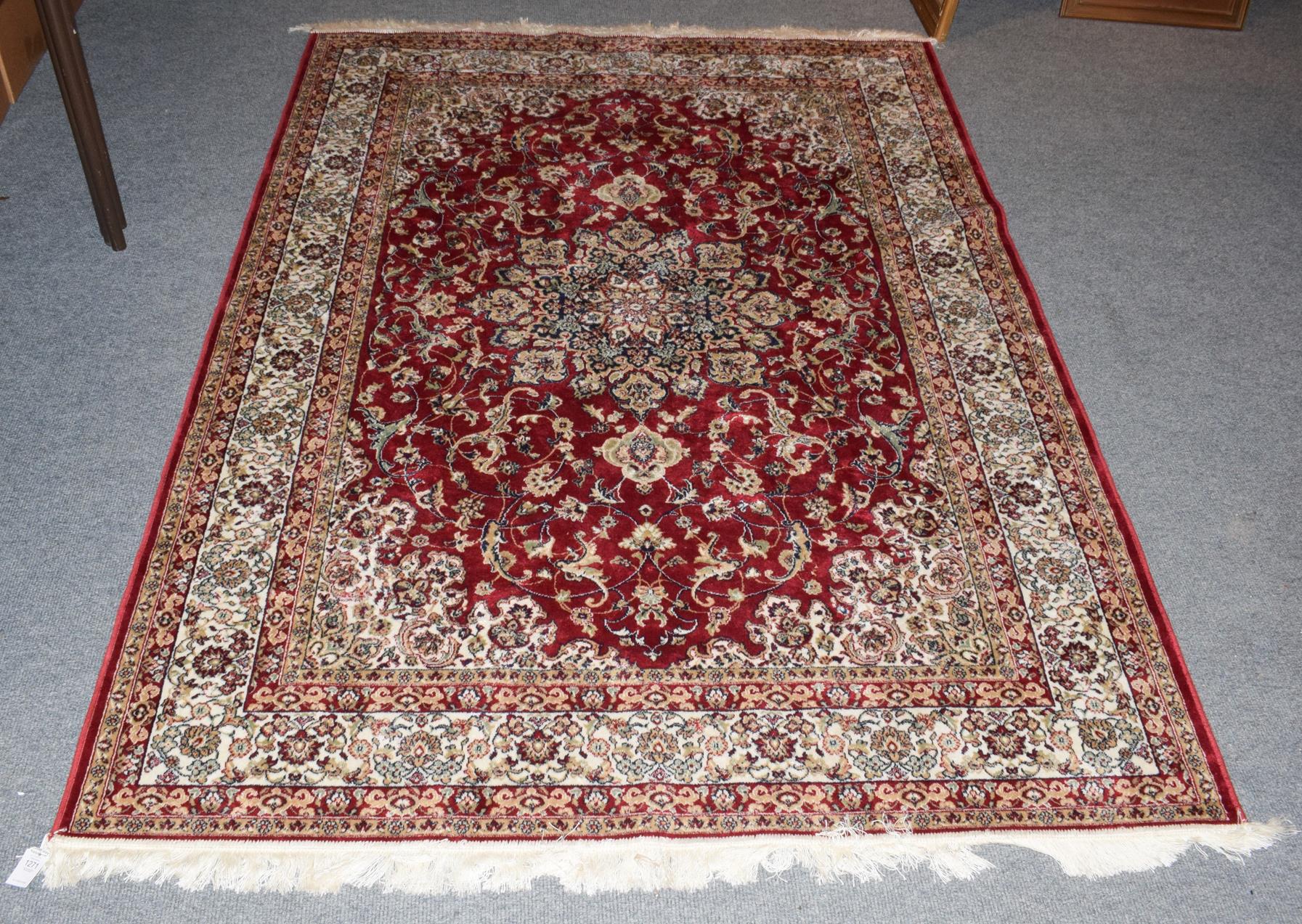 A machine made rug of Oriental design, the blood red floral field centred by medallion framed by