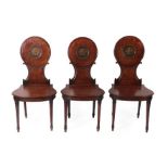 A Set of Three George III Mahogany Hall Chairs, late 18th century, each with circular and C scroll