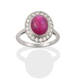A Ruby and Diamond Cluster Ring, the cabochon ruby in a white rubbed over setting, within a border