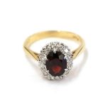 A garnet and diamond cluster ring, the oval cut garnet within a border of eight-cut diamonds, in