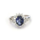 A sapphire and diamond cluster ring, the oval cut sapphire within a border of round brilliant cut