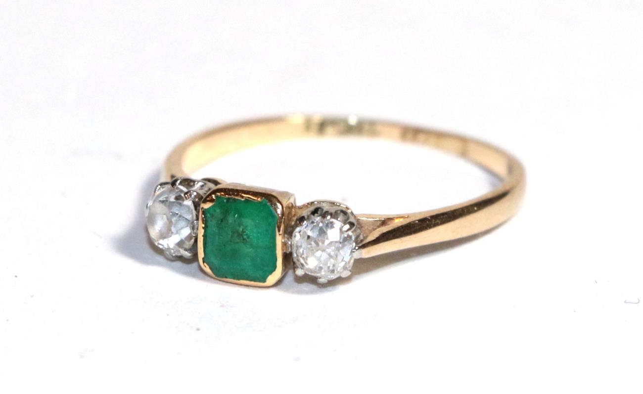 An emerald and diamond three stone ring, the emerald-cut emerald in a yellow rubbed over setting