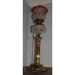 A Victorian brass Corinthian columnar oil lamp with clear glass reservoir and cranberry shade