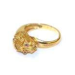 A lion mask ring, the lion mask motif with round cut ruby eyes in yellow collet settings, to a plain