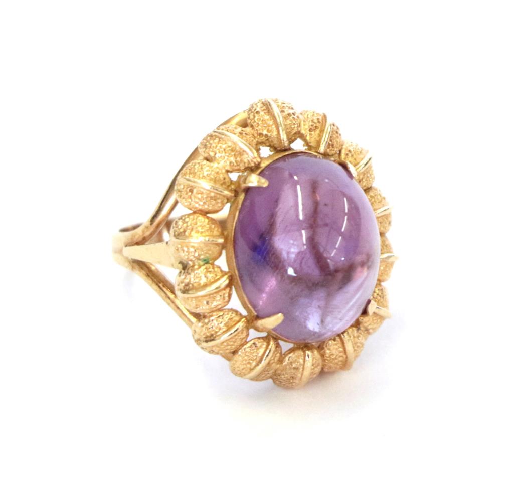 An amethyst ring, the oval cabochon amethyst in a yellow claw setting within a leaf motif border, to