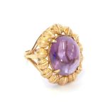 An amethyst ring, the oval cabochon amethyst in a yellow claw setting within a leaf motif border, to