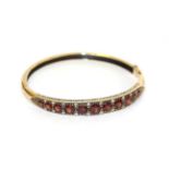 A 9 carat gold garnet and diamond hinged bangle, the eleven graduated garnets with eight-cut diamond