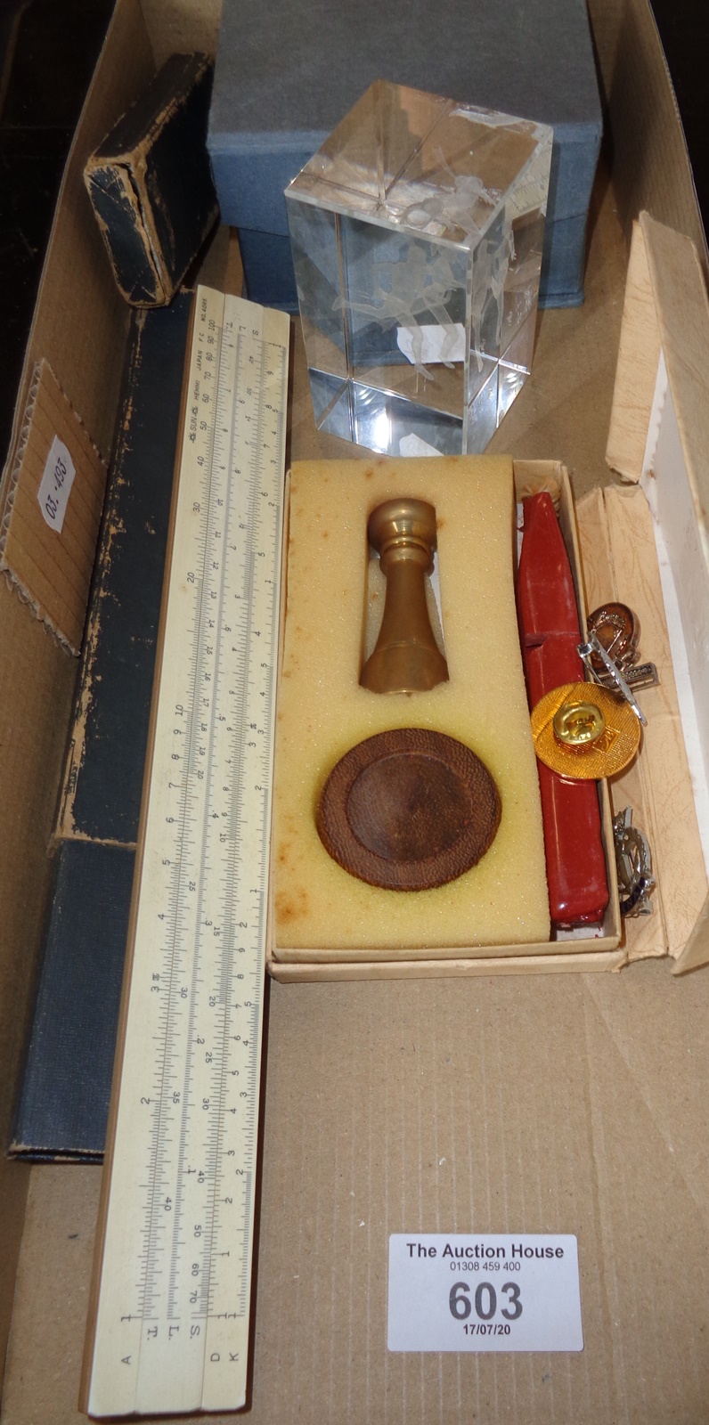 A brass seal with wax, a clear glass paperweight, four badges and a slide rule