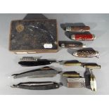 A vintage tin containing a quantity of penknives, cut throat razors, shell casings and similar.