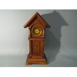 A mantel clock in the form of a grandfather clock with chalet-roof top, applied dyed decoration,