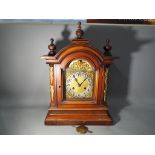 A large mantel clock in a stained beech or mahogany case, arched top surmounted by turned finials,