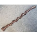 An African hardwood carved tribal staff or totem depicting a snake eating a lizard along the length,