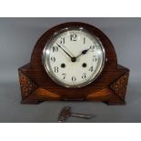 AN oak cased mantel clock with carved decoration, Arabic numerals to the dial,