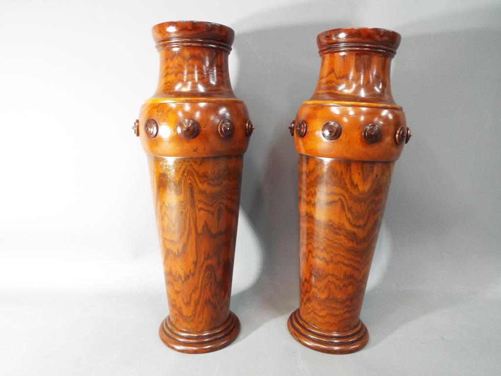 A pair of wooden vases, decorated with applied roundel motifs, approximately 34 cm (h).