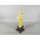 A Chinese soapstone carving depicting a lady standing, holding a fan with floral decoration,