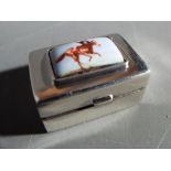 A silver pill box with enamelled equestrian decoration.
