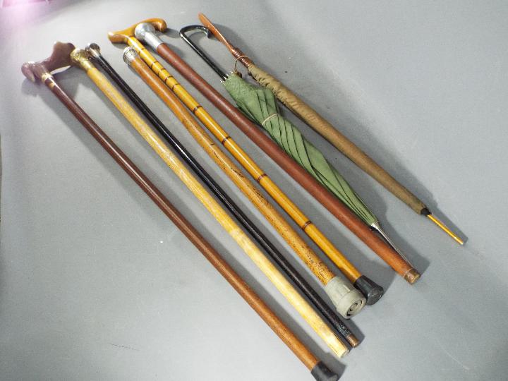 A mixed collection of walking sticks and umbrellas containing 2 silver topped walking sticks.