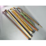 A mixed collection of walking sticks and umbrellas containing 2 silver topped walking sticks.