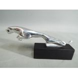 A chrome depiction of a Jaguar mounted on a wooden plinth