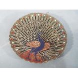 A circular dish / wall plaque with chased and enamel decoration depicting a peacock,