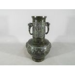 A Chinese / Japanese patinated, twin handled green bronze vase with relief decoration,