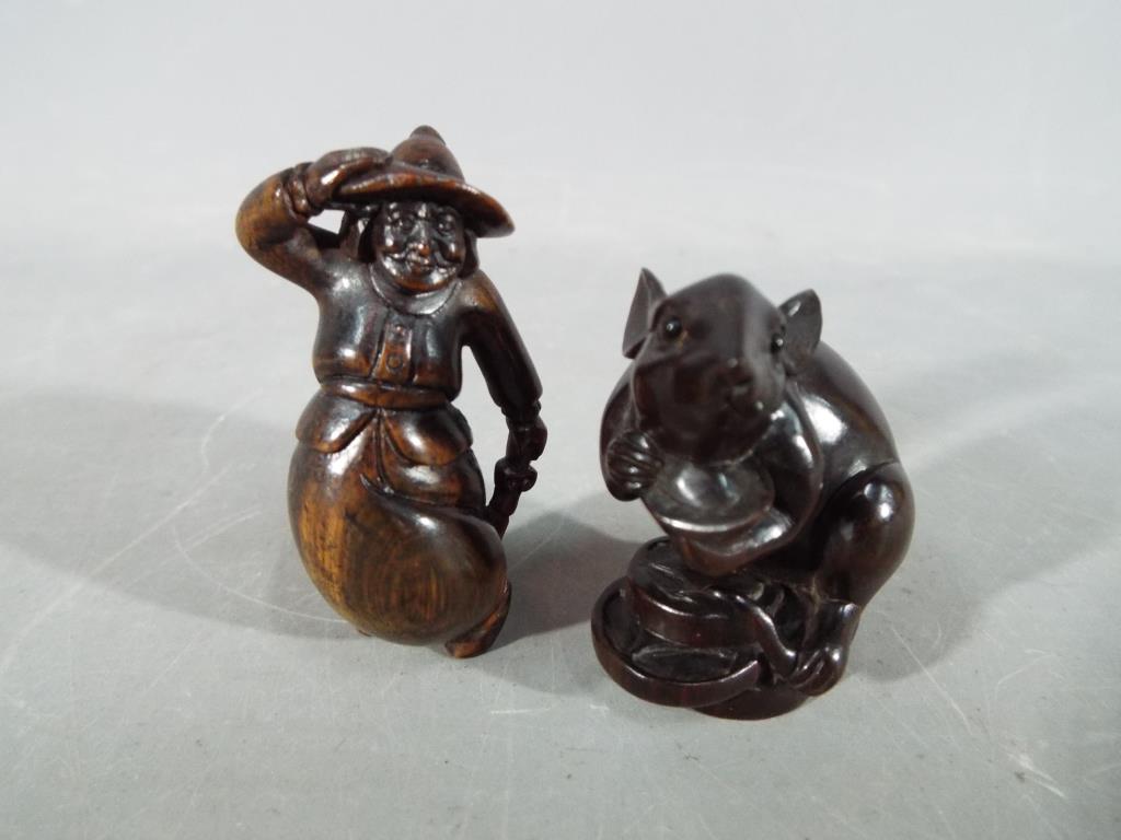 A vintage Japanese dark wood Netsuke depicting a large mouse or rat carrying its catch,