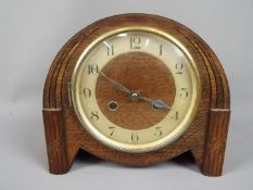 A wood cased mantel clock with carved detailing, Arabic numerals to a chapter ring,