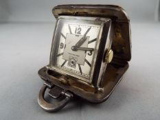 A small silver purse watch/ clock in a 36mm square cushion form case with brown leather covering,