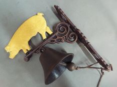 A wall mountable, cast iron bell surmounted with a depiction of a pig.