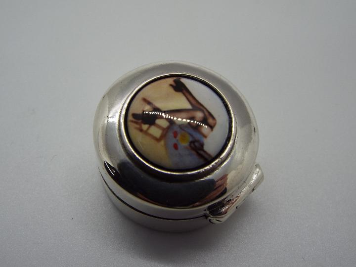 A silver pill box with painted enamel