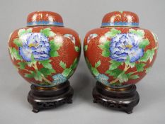 A pair of Chinese cloisonné ginger jars with floral decoration on a red ground,