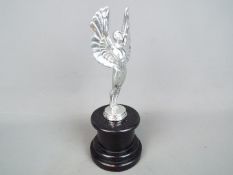 A chrome sculpture depicting a pair of angel wings set on a plinth,