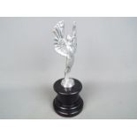 A chrome sculpture depicting a pair of angel wings set on a plinth,