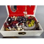 A mixed lot of costume jewellery in a cream jewellery box, including brooches, rings etc.