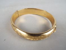A hallmarked 9ct gold bangle with safety chain (several dents and somewhat misshapen),