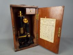 A 19th century lacquered brass monocular microscope on horseshoe base bearing plaque J. Woolley.