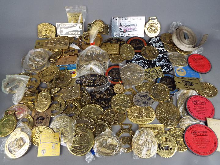 A box of steam fair and rally plaques, badges and similar, predominantly brass.