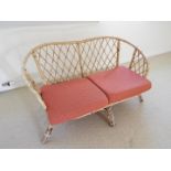 A two-seater bamboo couch with red upholstered seat cushions
