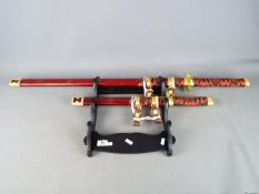 Two reproduction Japanese swords, longest approximately 101 cm, on wall mountable display stand.