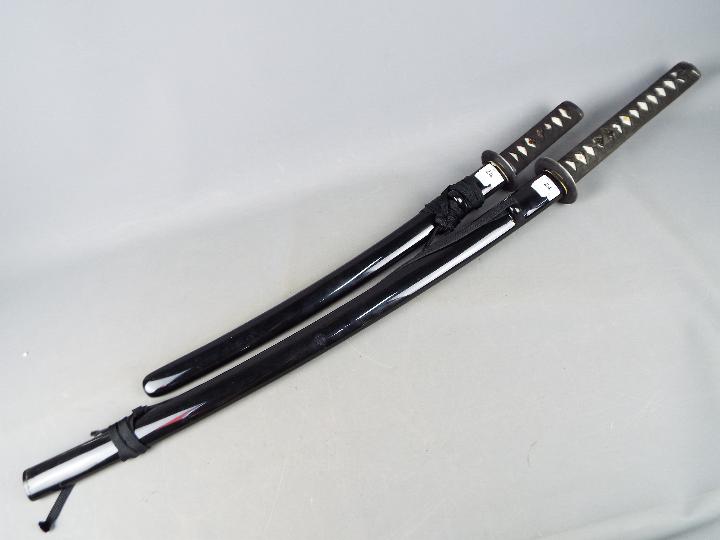 Two reproduction Japanese swords with black lacquered saya, longest approximately 109 cm.