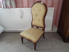 A button back nursing chair, the supports terminating in casters, beige upholstery,