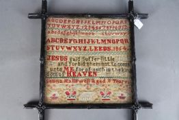 A framed needlework sampler with letters, numbers, biblical verse set between horizontal borders,