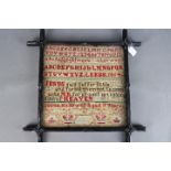 A framed needlework sampler with letters, numbers, biblical verse set between horizontal borders,