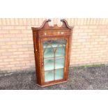 A George III mahogany bow-fronted hanging corner cupboard with broken swan-neck pediment above an