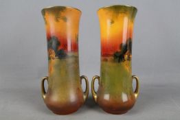 Royal Doulton - A set of two twin handled, elongated vases decorated with rural cottage scenes,