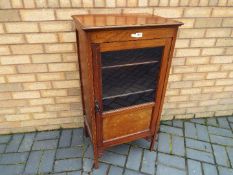 An Edwardian mahogany cabinet, the glazed door opening to reveal a four-tier shelved interior,